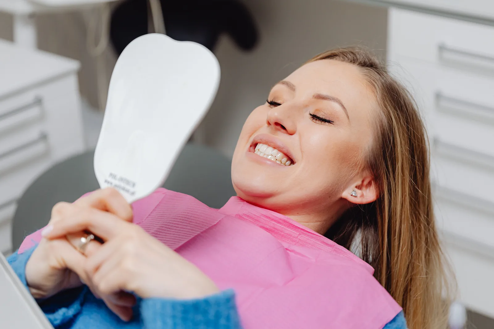 Mulher sorrindo em consultório odontológico, segurando um espelho