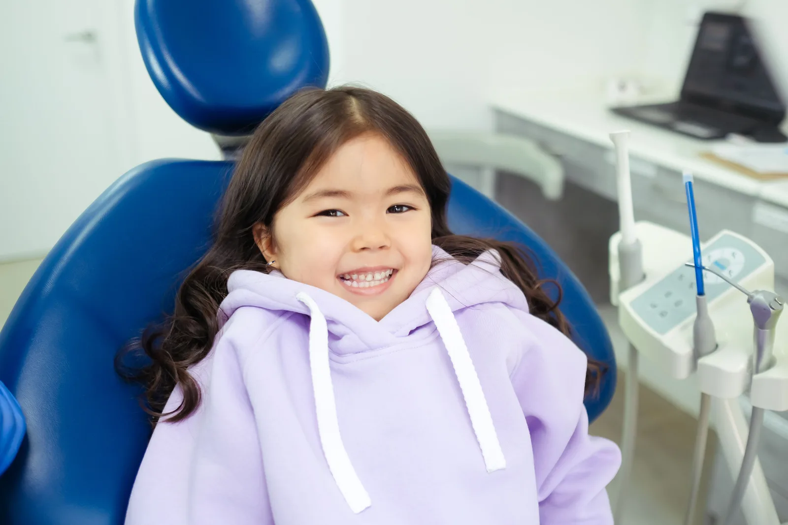Criança sorrindo, sentada na cadeira odontológica