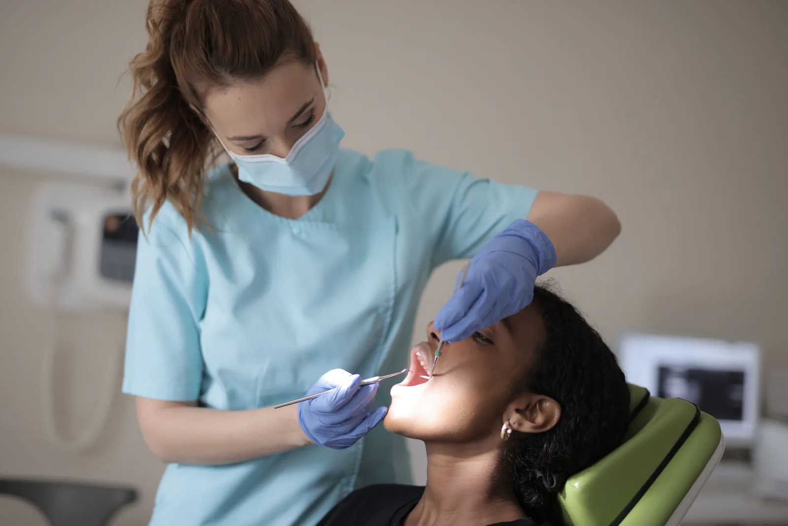 Dentista de jaleco azul examinando uma paciente na cadeira
