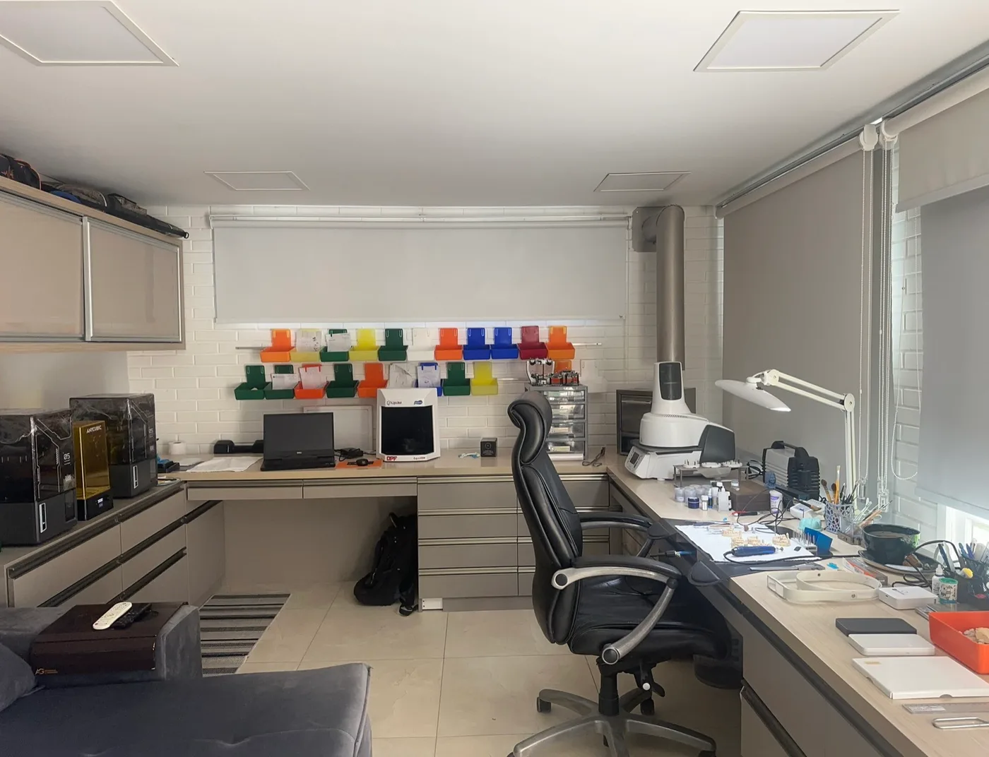 Bancada do laboratório de prótese, com microscópio, monitor e escala de cores na parede
